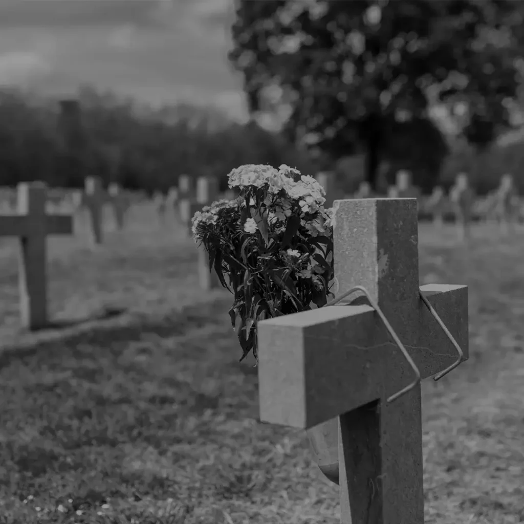 Cross-Shaped Headstone With Flowers In A Cemetery